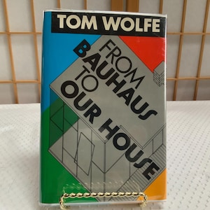 May include: A hardcover book titled From Bauhaus to Our House by Tom Wolfe. The dust jacket features a black header with white text, and a graphic illustration of a building structure set against vibrant blue, red, green, and orange panels.