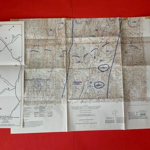 May include: A vintage topographical map of Fort Benning, Georgia, with detailed contour lines, roads, and labeled areas. The map is folded and shows the "United States Army Infantry School." The map is on a red background.