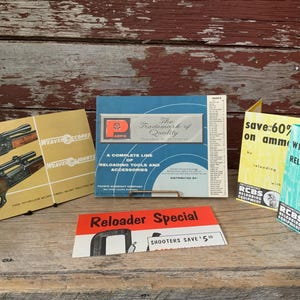 May include: A collection of vintage reloading equipment and supplies, including a pamphlet titled "The Trademark of Quality" with a red "P" logo, a pamphlet titled "Why Reload?" with a question mark, and a pamphlet titled "Reloader Special" with the text "Shooters Save 50".