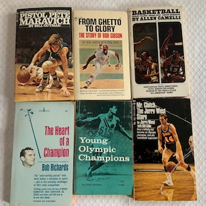 May include: A collection of six vintage sports books. Titles include "Pistol Pete Maravich," "From Ghetto to Glory," "Basketball," "The Heart of a Champion," "Young Olympic Champions," and "Mr. Clutch: The Jerry West Story." The books feature images of athletes.