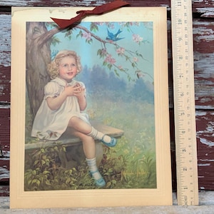 May include: A vintage print of a young girl in a white dress sitting on a bench under a tree with a bluebird flying overhead. The girl is looking up at the bird with a smile on her face. The print is framed in a cream-colored mat.