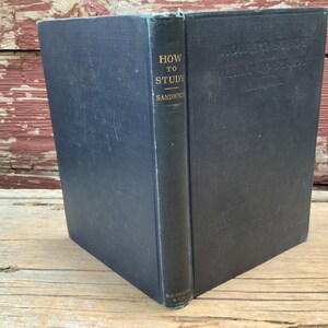 May include: A navy blue hardcover book titled "How to Study" by  D.C.  Heath & Co.  The book is sitting on a wooden surface.