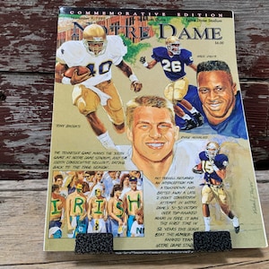 May include: A commemorative edition program for a Notre Dame football game. The cover features illustrations of players in action, including a player wearing a gold jersey with the number 40, a player wearing a blue jersey with the number 26, and a player wearing a blue jersey with the number 15. The program is dated November 9, 1991, and includes the text "Notre Dame" and "Commemorative Edition".