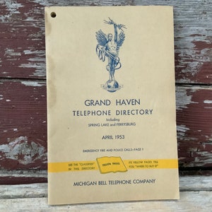 May include: A vintage Grand Haven Telephone Directory from April 1953, including Spring Lake and Ferrysburg. The cover features a blue illustration of a winged figure holding a lightning bolt, standing on a globe. The text "YELLOW PAGES" is highlighted in yellow.