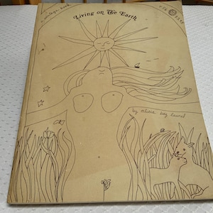 May include: A vintage book titled "Living on the Earth" with a hand-drawn illustration. The cover features a sun with a face, a woman, and animals. The book is tan with black line art.