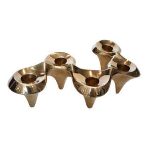 May include: A gold-toned metal candle holder with five candle cups. The holder has a unique, organic shape with a wavy design.