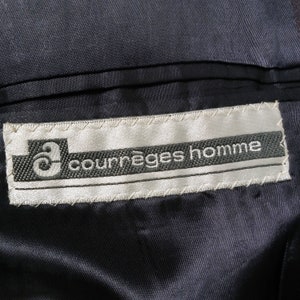 May include: A white label with black stitching and the text "Courr&egrave;ges homme" in black lettering.