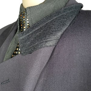 May include: A dark gray blazer with a black and gold patterned tie and a gray fleece lining. The blazer is folded over to show the lining.