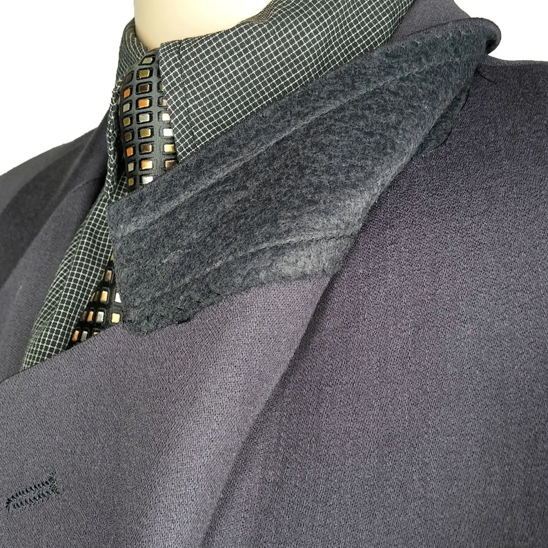 May include: A dark gray blazer with a black and gold patterned tie and a gray fleece lining. The blazer is folded over to show the lining.