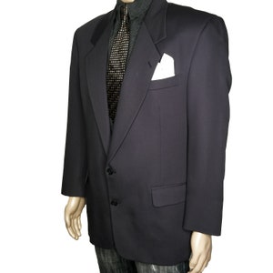 May include: A dark blue blazer with a single button closure and a pocket on the left side. The blazer has a white pocket square and a black patterned tie.