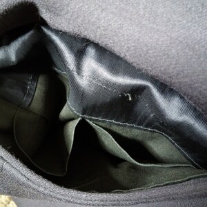 May include: The inside of a black hat with a black satin lining and two pockets. The pockets are made of a dark green fabric.
