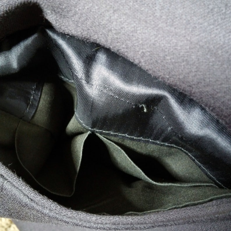 May include: The inside of a black hat with a black satin lining and two pockets. The pockets are made of a dark green fabric.