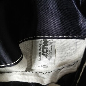 May include: A white label sewn into a black garment with the text "Union Made in USA" and "Amalgamated Textile Workers Union" printed on it. The label also features the word "ACTWU" in a stylized font.