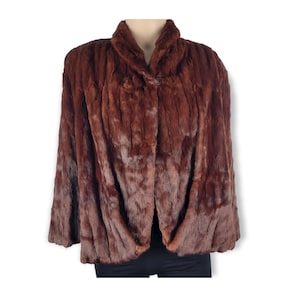 Könnte beinhalten: Eine braune Pelzjacke mit Knopfverschluss. Die Jacke hat einen Kragen und lange Ärmel.