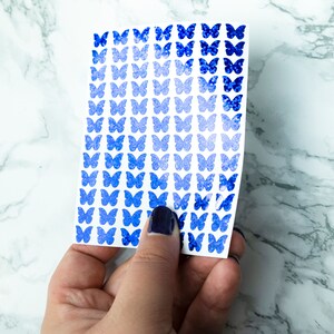 May include: A sheet of blue butterfly stickers with a gradient effect, ranging from light blue to dark blue. The stickers are arranged in rows on a white background.
