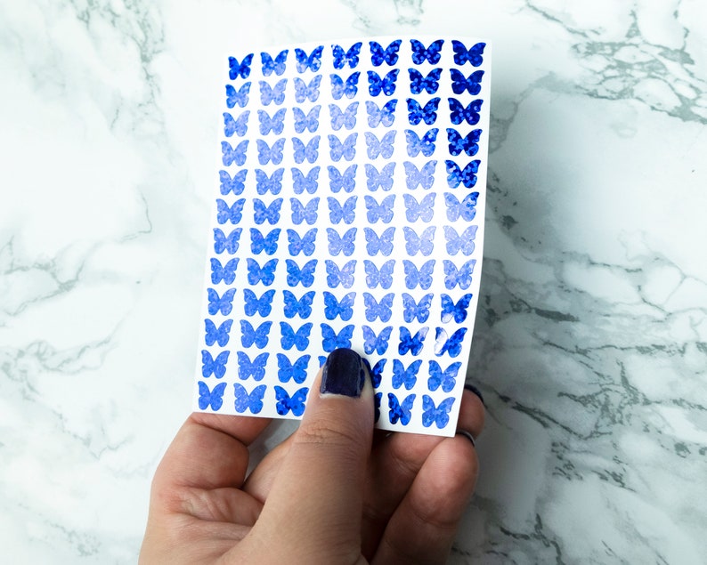 May include: A sheet of blue butterfly stickers with a gradient effect, ranging from light blue to dark blue. The stickers are arranged in rows on a white background.