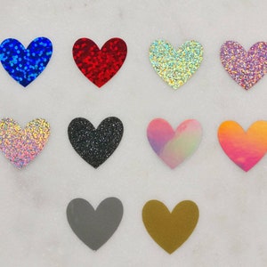 May include: Ten heart-shaped craft supplies in various colors and finishes, including glitter, iridescent, and solid colors. The hearts are arranged in two rows of five.