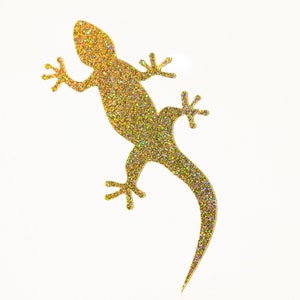 May include: A gold glitter gecko silhouette against a white background.