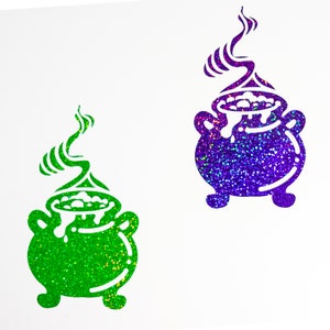 Könnte beinhalten: Zwei Kessel-Aufkleber mit grünem und violettem Glitzer-Finish. Die Kessel sind mit sprudelnder Flüssigkeit gefüllt und aus ihnen steigt Dampf auf.