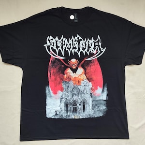 May include: A black short-sleeve t-shirt featuring a graphic print of a winged figure standing behind a gothic cathedral. The text SEPULTURA appears in a stylized white font at the top, and the words BESTIAL DEVASTATION are printed at the bottom.