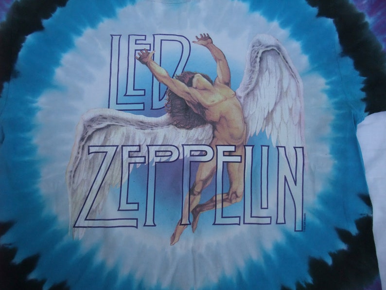 May include: Tie-dye t-shirt featuring the Led Zeppelin band logo and a graphic of a winged figure. The shirt has a blue and white spiral design. The band's name is in a blue outline font.