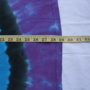 May include: A tie-dye textile with a color gradient of blue, black, and purple. A yellow measuring tape is laid across the fabric, showing a length of approximately 13 inches.