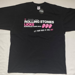 May include: A black short-sleeve t-shirt featuring white and pink text that reads T-Mobile Presents ROLLING STONES LICKS EUROPEAN TOUR 2003 LET YOUR ROCK 'N' ROLL OUT, accompanied by three pink tongue and lip graphic icons on the front chest area.