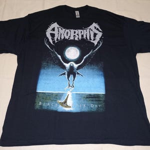 May include: Black t-shirt featuring the band name "Amorphis" in white, gothic-style lettering above a graphic of a bird in front of a full moon. The text "Black Winter Day" is below the bird. The shirt is made of a soft material.