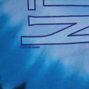 May include: A blue tie-dye t-shirt with the Led Zeppelin logo in dark blue. The text "&copy;1975 Led Zeppelin" is printed at the bottom. The background has a cloudy, tie-dye effect.