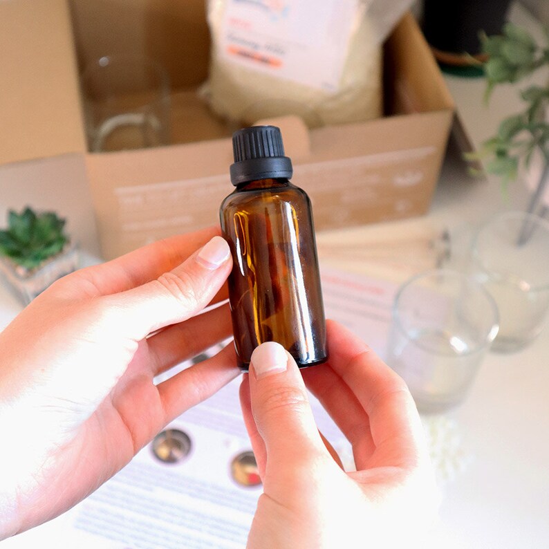 May include: A small amber glass bottle with a black lid. The bottle is being held by a person's hands.