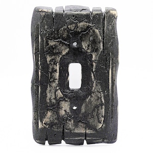 May include: Black light switch cover made to look like weathered wood. The cover has a rectangular shape with a single switch opening.
