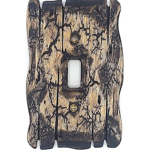 Peut inclure: Un cache-interrupteur en bois rustique avec une ouverture pour un seul interrupteur. Le couvercle est fait de plusieurs planches de bois avec un aspect vieilli et brûlé. Le grain du bois est visible, et le couvercle est fixé avec deux vis en laiton.