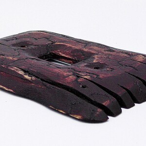 May include: A dark brown wooden light switch cover with a rough, textured surface. The cover is made of multiple thin pieces of wood that have been joined together.