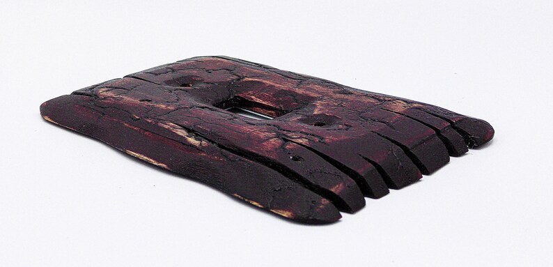 May include: A dark brown wooden light switch cover with a rough, textured surface. The cover is made of multiple thin pieces of wood that have been joined together.