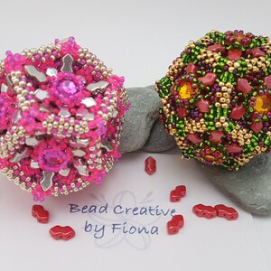 May include: Two beaded sphere ornaments. One is hot pink with silver and magenta accents. The other is green, gold, and red. The ornaments are on a gray stone with red beads scattered around. The text "Bead Creative by Fiona" is visible.