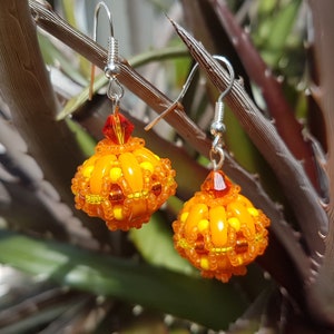 May include: A pair of orange and yellow beaded earrings with silver hooks. The earrings are shaped like small spheres and have a textured surface.