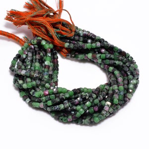 Może przedstawiać: Sznur zielonych, czarnych i różowych koralików z kamieni szlachetnych. Koraliki są fasetowane i mają kwadratowy kształt. Sznur ma około 46 cm długości.