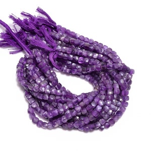 Może przedstawiać: Szereg fioletowych koralików z ametystu. Koraliki są fasetowane i mają kwadratowy kształt. Koraliki są nawleczone na nić i mają frędzle na końcu.
