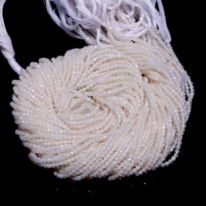 Puede incluir: Una hebra de cuentas de piedras preciosas blancas, probablemente piedra lunar, con un acabado facetado. Las cuentas están enhebradas en un hilo blanco y tienen aproximadamente 2 mm de diámetro.