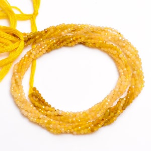 May include: Strands of faceted yellow beads, varying in shades from pale to deep gold, are arranged in a circular pattern. Bright yellow cords are tied at the top, suggesting a necklace or jewelry component. The beads have a sparkling, polished appearance.