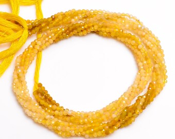 May include: Strands of faceted yellow beads, varying in shades from pale to deep gold, are arranged in a circular pattern. Bright yellow cords are tied at the top, suggesting a necklace or jewelry component. The beads have a sparkling, polished appearance.