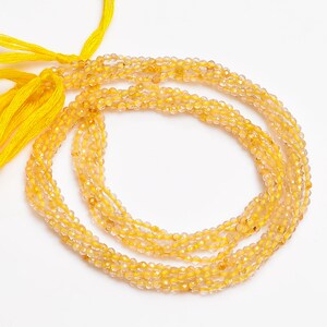K&ouml;nnte beinhalten: Eine Str&auml;hne gelber Citrin-Edelsteinkugeln. Die Kugeln sind facettiert und haben ein durchscheinendes Aussehen. Die Str&auml;hne ist etwa 45 cm lang und auf einer durchsichtigen Gummikordel aufgef&auml;delt.