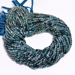 May include: A strand of blue gemstone beads, each bead is faceted and has a slightly irregular shape. The beads are strung on a cord with a blue tassel at the end.