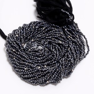 Pode incluir: Um fio de contas de pedra preciosa facetadas pretas. As contas são pequenas e redondas, e têm um acabamento brilhante e metálico.