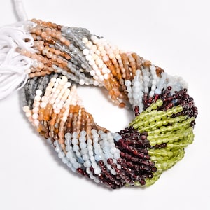 May include: A strand of gemstone beads in various colors, including green, brown, red, blue, and white. The beads are small and round, and they are strung together on a white thread.