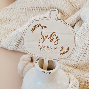 May include: Wooden pumpkin-shaped sign with the text "Seb's Pumpkin Patch" in a cursive font. The sign is decorated with small leaf designs.