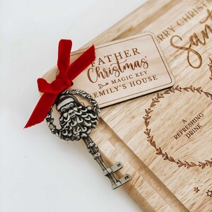 May include: A wooden cutting board with a Santa Claus key and a tag that reads "Father Christmas - Magic Key - Emily's House". The board is engraved with a wreath and the text "A Refreshing Drink".