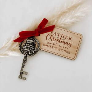 May include: A wooden sign with the text "Father Christmas Magic Key Emily's House" and a silver key with a Santa Claus head on the top. The key is tied with a red ribbon.