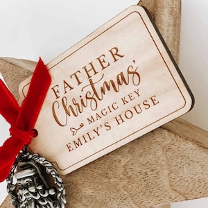 May include: A wooden star ornament with a red ribbon and a silver Santa charm. The ornament has a tag that reads "Father Christmas, Magic Key Emily's House".