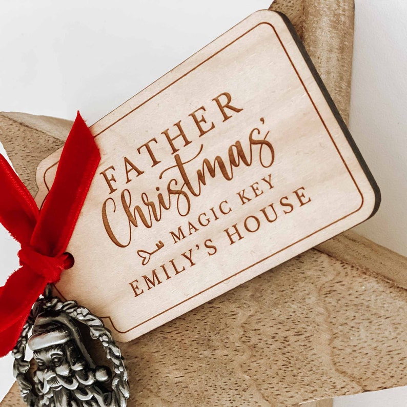 May include: A wooden star ornament with a red ribbon and a silver Santa charm. The ornament has a tag that reads "Father Christmas, Magic Key Emily's House".